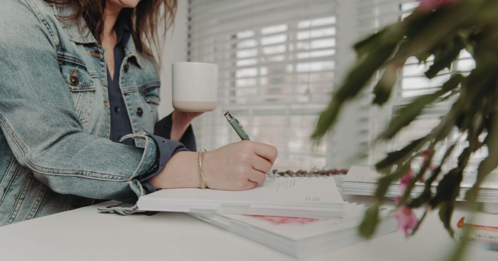 Holding a cup of coffee while writing in the In Season Planner