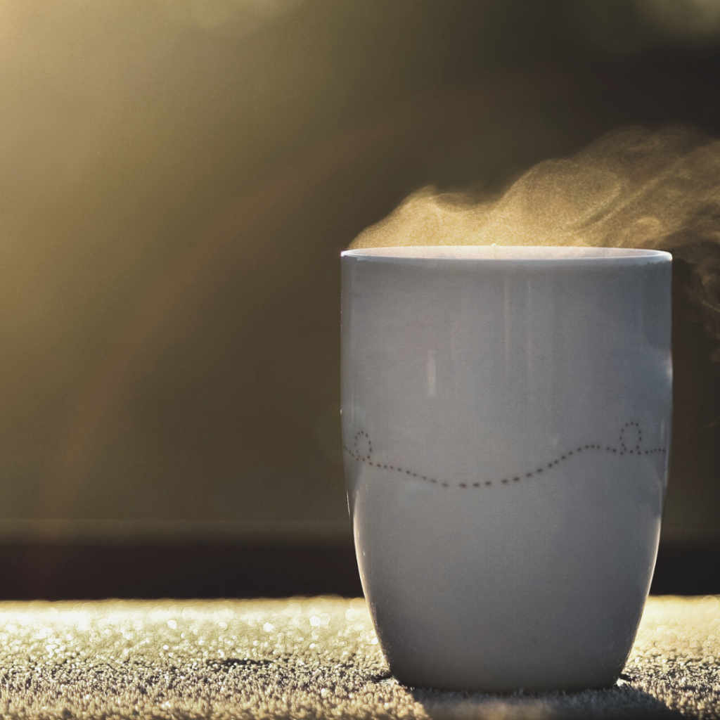 morning routine with a cup of coffee with steam coming out on a railing outside with the sun rising in the background